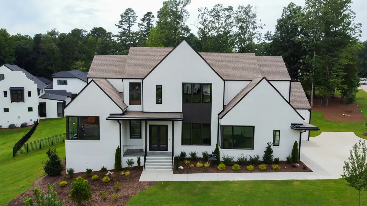 A bright new white farmhouse with a dark roof and a fresh lawn